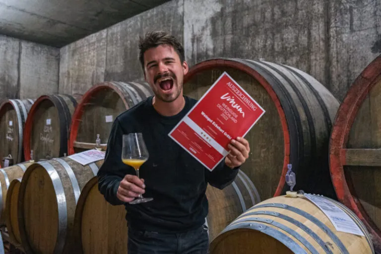 Image on Johannes Gröhl holding a diploma in his wine cellar at Gröhl Winery.