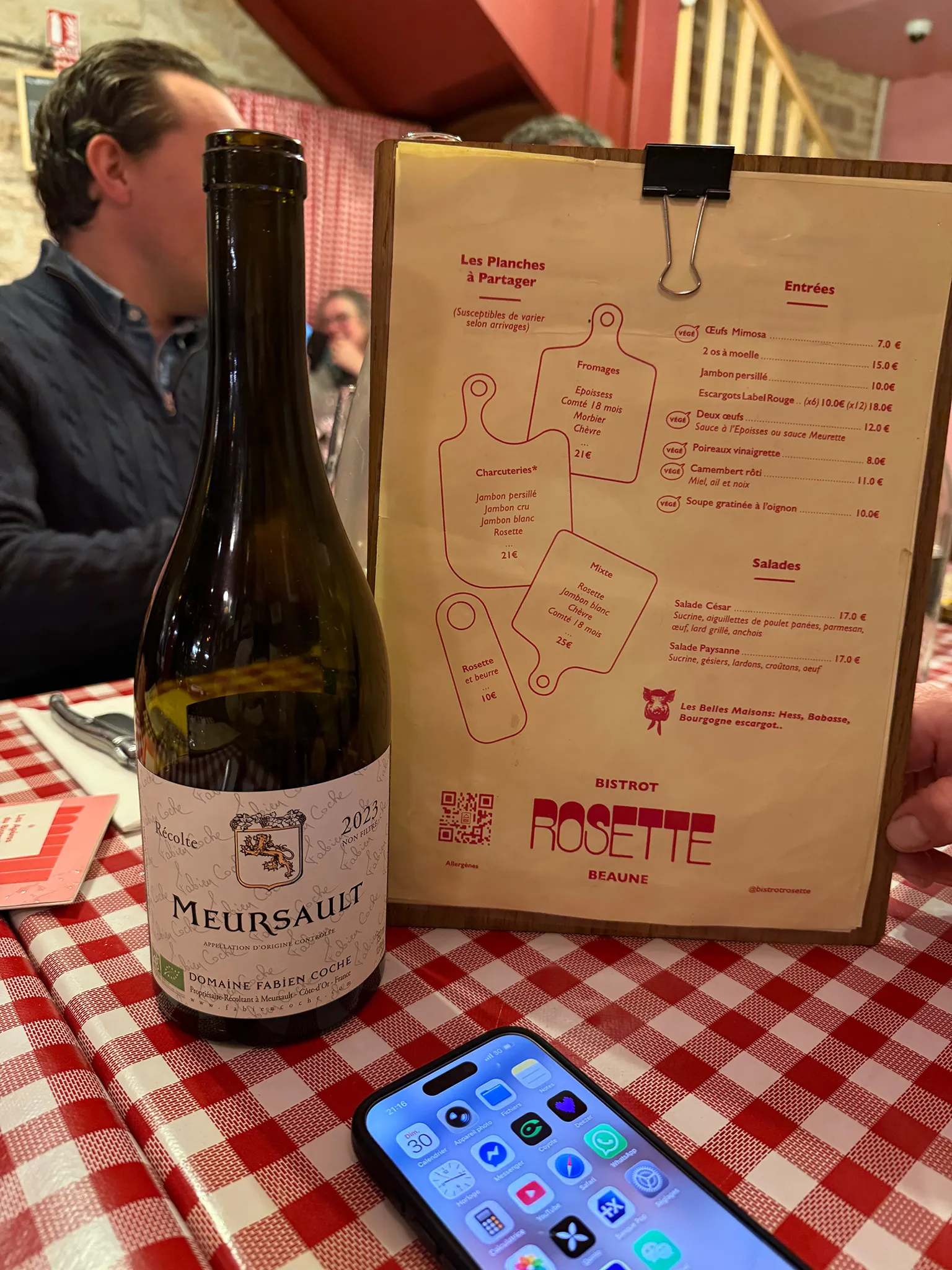 Vad snackar du om? A Meursault-bottle standing on a red and white checkered table cloth with a menu but at the side in a bistro.